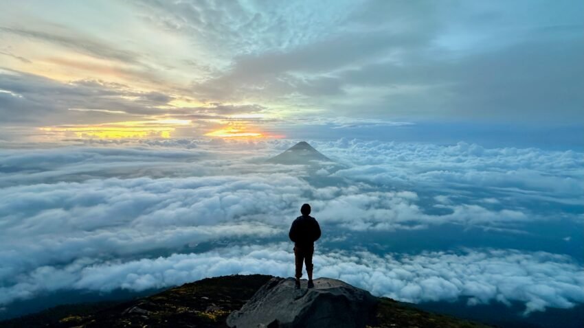 Man overlooking sea of clouds during sunrise while a volcano pokes thru!